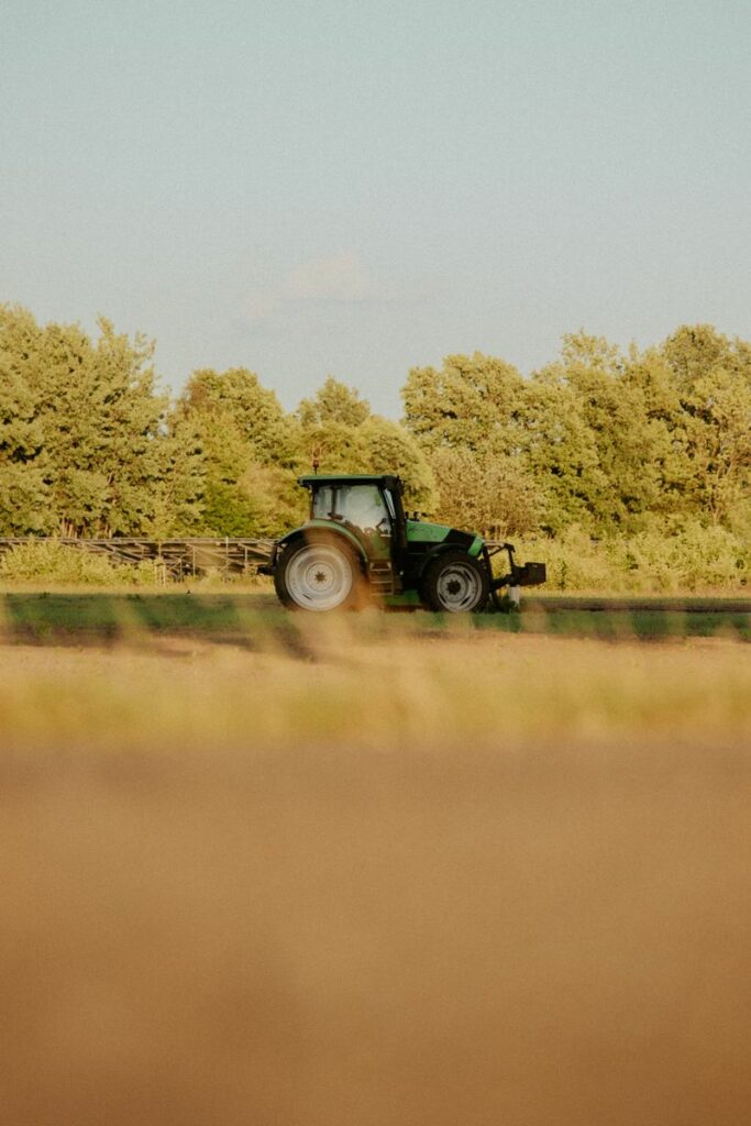 Green tractor working on a farm field in sunny weather. Ideal for agriculture and rural themes.