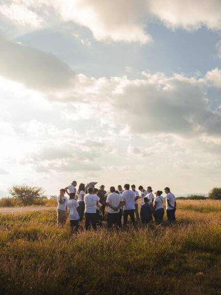 A group of people gathered in a sunny field under a cloudy sky, creating a serene scene.