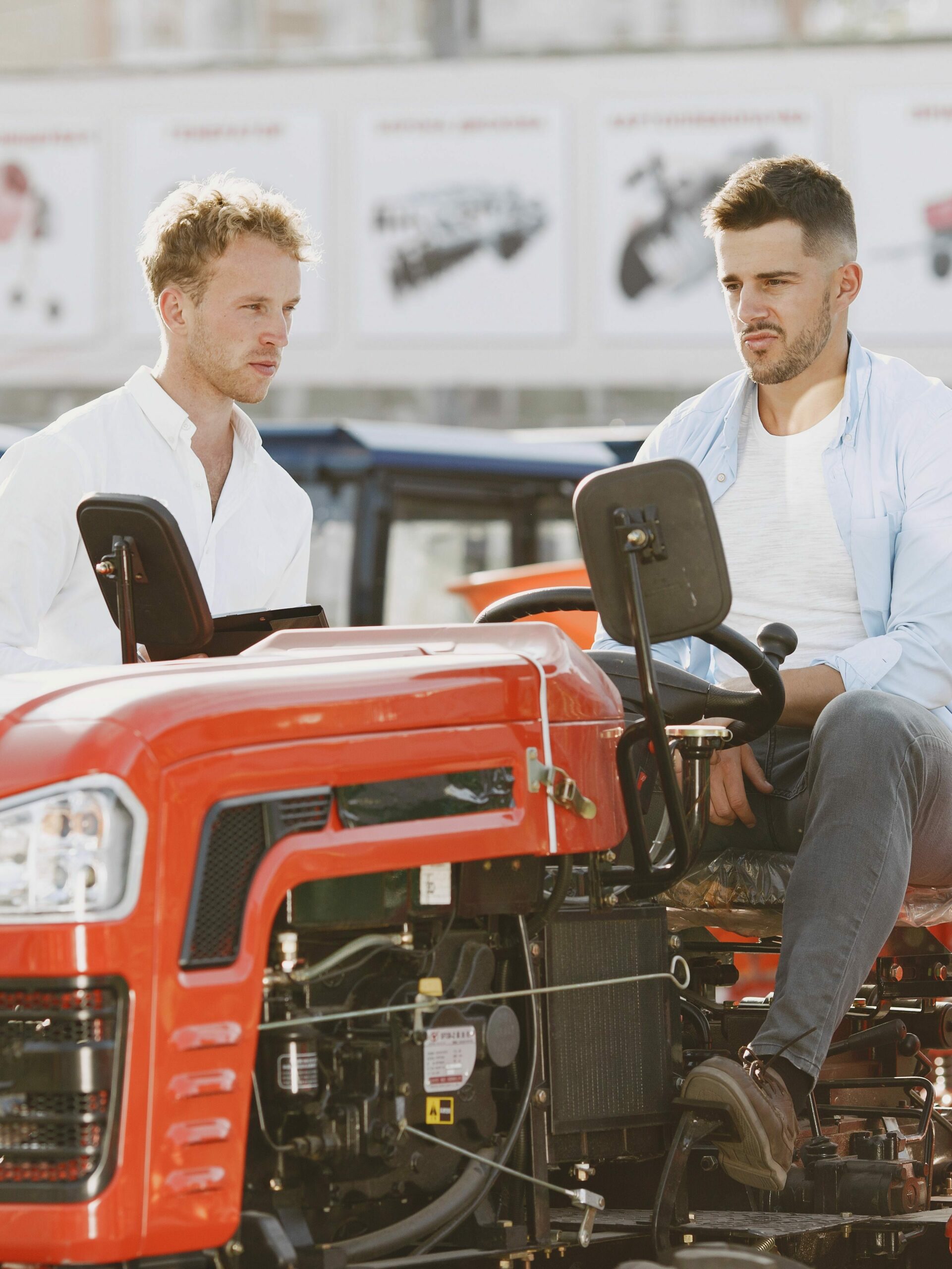 Two men in casual attire inspecting red tractors in an outdoor showroom.